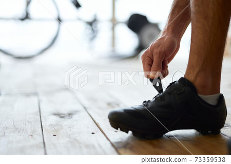 Young man putting on sports shoes before training at home Young man putting on sports shoes before training at home 73359538