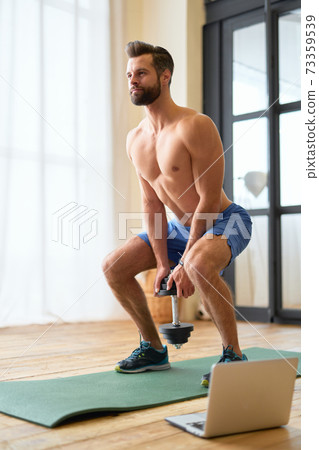Handsome young man doing exercise with dumbbell at home Handsome young man doing exercise with dumbbell at home 73359539