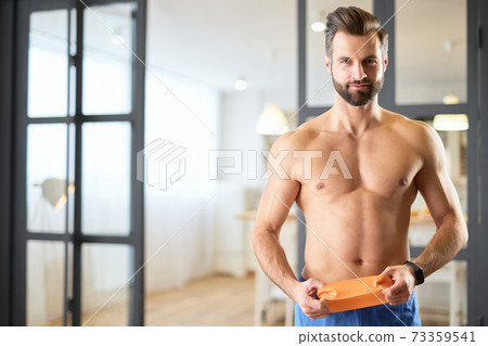 Handsome young man with perfect abs holding resistance band 73359541