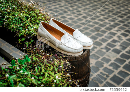 White leather moccasins. Photo on the street next to the flowers. Trendy white loafers. Fashionable women's leather shoes. White leather moccasins. Photo on the street next to the flowers. Trendy white loafers. Fashionable women's leather shoes. 73359632