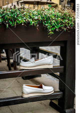 White leather moccasins. Photo on the street next to the flowers. Trendy white loafers. Fashionable women's leather shoes. White leather moccasins. Photo on the street next to the flowers. Trendy white loafers. Fashionable women's leather shoes. 73359633