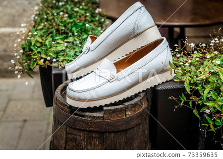 White leather moccasins. Photo on the street next to the flowers. Trendy white loafers. Fashionable women's leather shoes. White leather moccasins. Photo on the street next to the flowers. Trendy white loafers. Fashionable women's leather shoes. 73359635