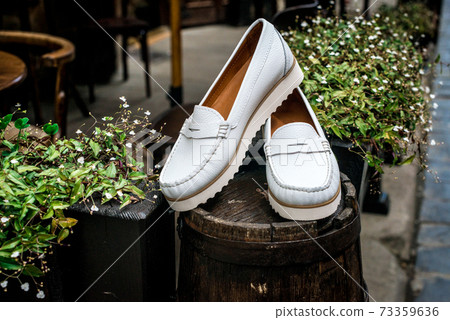 White leather moccasins. Photo on the street next to the flowers. Trendy white loafers. Fashionable women's leather shoes. 73359636