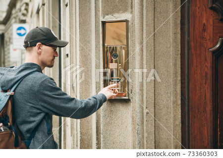 Man presses a doorphone button Man presses a doorphone button 73360303
