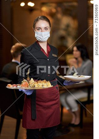 Serious woman in waitress uniform posing with plates of food 73360969