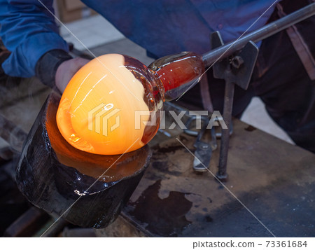 Artisan hands working with hot malleable glass on glassblower whistle. 73361684