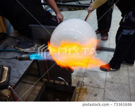 Glass artist forms the scorching glass with heats it with a gas burner Glass artist forms the scorching glass with heats it with a gas burner 73361686
