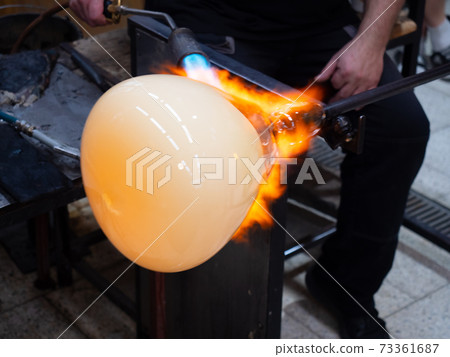 Glass artist forms the scorching glass with gas burner torch. 73361687
