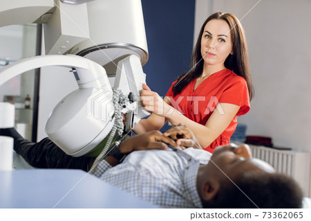 Portrait of young attractive woman doctor, looking at camera, while providing lithotripsy procedure for her male African American patient with modern ultrasonic lithotriptor to break up stones Portrait of young attractive woman doctor, looking at camera, while providing lithotripsy procedure for her male African American patient with modern ultrasonic lithotriptor to break up stones 73362065