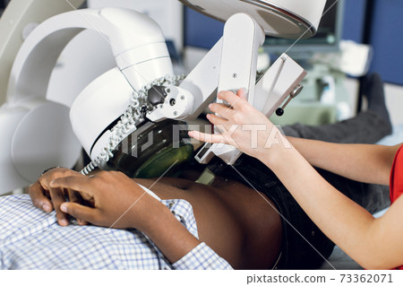 Close up cropped image of lying African man patient having procedure of lithotripsy. Hands of female doctor working with modern ultrasonic lithotripter to crush kidney or ureter stones Close up cropped image of lying African man patient having procedure of lithotripsy. Hands of female doctor working with modern ultrasonic lithotripter to crush kidney or ureter stones 73362071