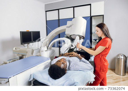 Treatment of urethral stones by non-invasive Extracorporeal Shock Wave Lithotripsy. Woman doctor providing the kidney stones lithotripsy for her male African patient in modern clinic Treatment of urethral stones by non-invasive Extracorporeal Shock Wave Lithotripsy. Woman doctor providing the kidney stones lithotripsy for her male African patient in modern clinic 73362074