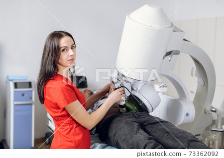 Close up portrait of young woman doctor in red uniform, working with modern ultrasonic lithotripter machine, making lithotripsy for kidney stones for male African patient in modern urology center 73362092
