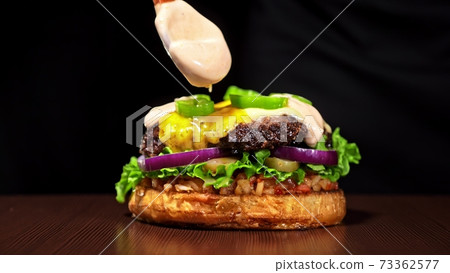 Craft burger is cooking on black background. Consist: sauce salsa, lettuce, red onion, pickle, cheese, chilli green pepper, bun, marbled meat beef. Craft burger is cooking on black background. Consist: sauce salsa, lettuce, red onion, pickle, cheese, chilli green pepper, bun, marbled meat beef. 73362577