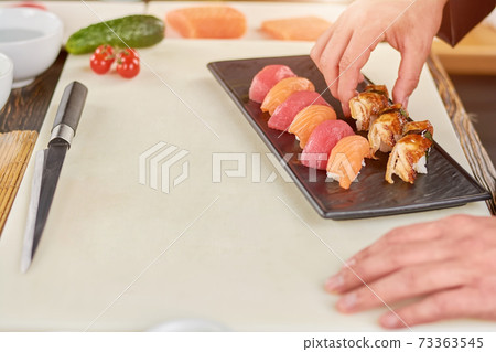 Chef hands placing nigiri sushi on plate. 73363545