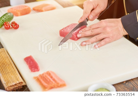 Chef cutting raw tuna on cutting board. 73363554