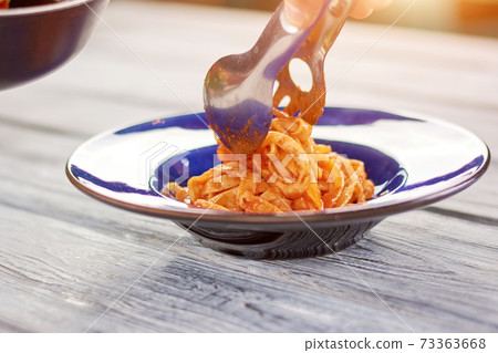 Kitchen stainless tongs putting pasta on plate. Kitchen stainless tongs putting pasta on plate. 73363668
