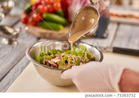 Chef pouring sauce on mixed salad. 73363732