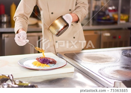 Chef pouring orange sauce on meat. Chef pouring orange sauce on meat. 73363885