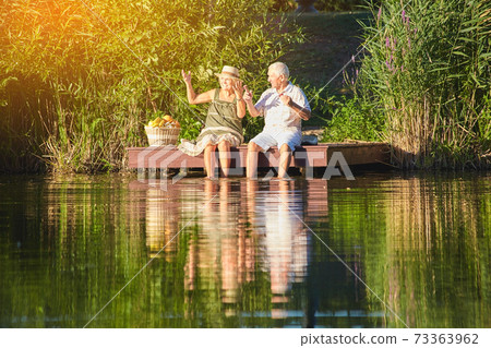 Senior couple sitting near water. Senior couple sitting near water. 73363962