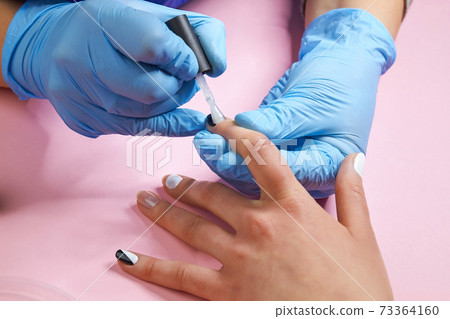 Beautician applying varnish on index nail. Beautician applying varnish on index nail. 73364160