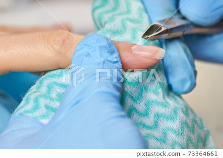 Beautician in gloves cutting cuticle to client. 73364661