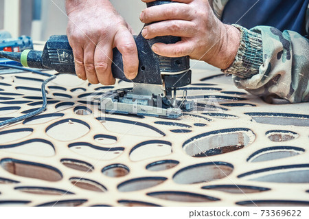 Decorative partition wall with floral pattern. Carpenter cuts holes in MDF using a jigsaw Decorative partition wall with floral pattern. Carpenter cuts holes in MDF using a jigsaw 73369622