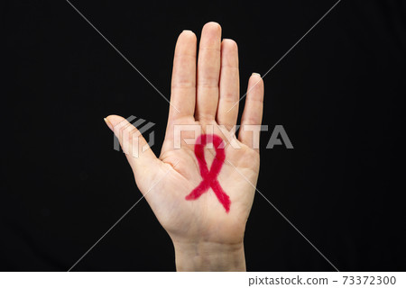 A female hand reaches up with a red awareness ribbon drawn on the palm. Black background. World AIDS day concept 73372300