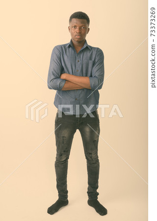 Full body shot of young black African man standing with arms crossed against white background 73373269