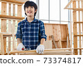 Portrait of happy Asian boy standing in carpentry workshop and holding hammer at home. 73374817