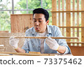 Man blowing sawdust out of timber wood in carpentry workshop. 73375462
