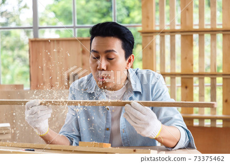Man blowing sawdust out of timber wood in carpentry workshop. Man blowing sawdust out of timber wood in carpentry workshop. 73375462