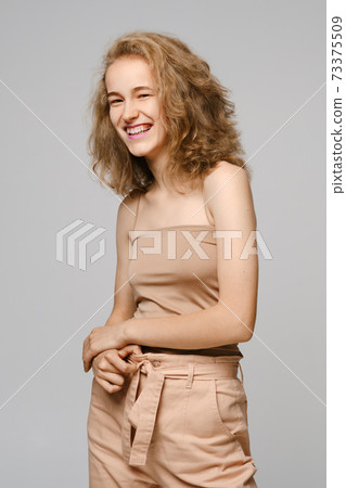 Cute girl with blonde hair in tank top and trousers smiling and laughing 73375509
