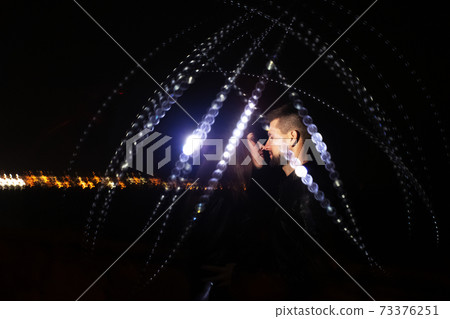 Lovers stand at night against the background of freezelight. Drawing light for loving people. The concept of magic in relationships and beautiful love. 73376251