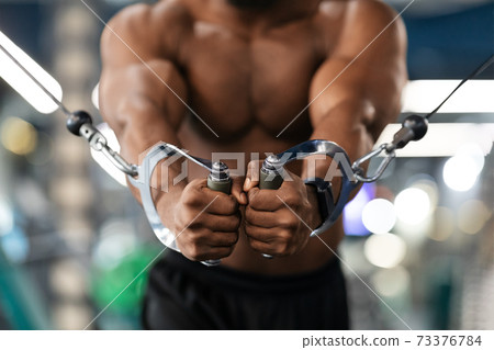 Unrecognizable black athlete training triceps on crossover exerciser in gym 73376784