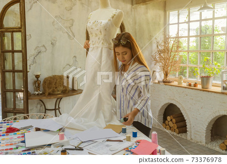 Asian female fashion designers adjusting dress on model in the studio Asian female fashion designers adjusting dress on model in the studio 73376978