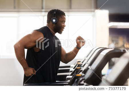Muscular black man in modern wireless headphones running at gym 73377170