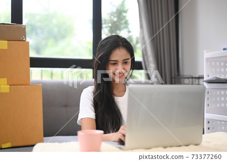 Small business owner working with laptop and sitting in living room surrounded by boxes. SME concept. 73377260