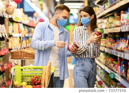 Young couple in disposable face masks shopping in supermarket Young couple in disposable face masks shopping in supermarket 73377358