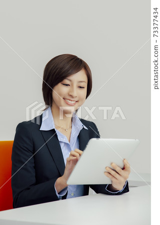 Business woman operating a tablet PC with a smile 73377434