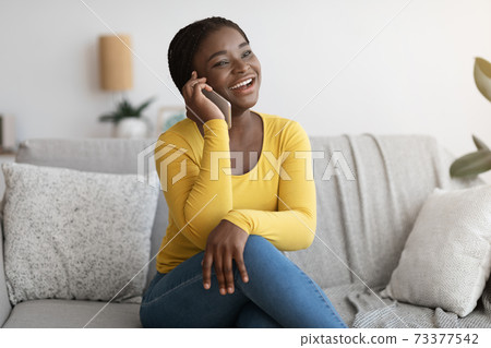 Positive African American Lady Talking On Mobile Phone At Home, Enjoying Conversation Positive African American Lady Talking On Mobile Phone At Home, Enjoying Conversation 73377542