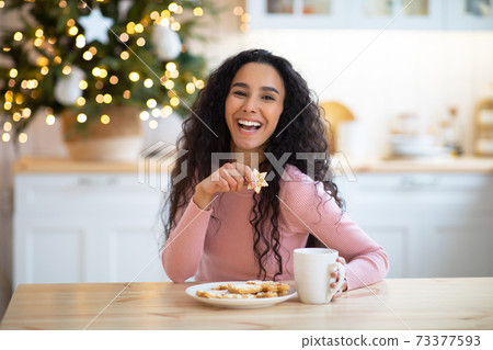 Christmas Snack. Joyful woman enjoying holiday cookies and hot chocolate in kitchen Christmas Snack. Joyful woman enjoying holiday cookies and hot chocolate in kitchen 73377593