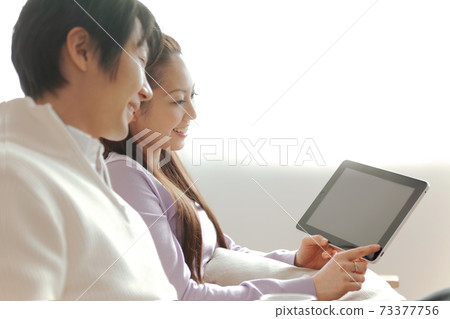 一對夫婦坐在沙發上看到一台平板電腦的屏幕 73377756