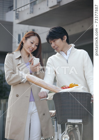 男子推著自行車,婦女看著智能手機 男子推著自行車,婦女看著智能手機 73377887