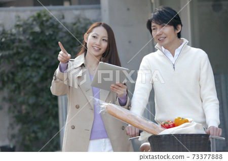 一個男人推著自行車和一個女人拿著一台平板電腦用手指 一個男人推著自行車和一個女人拿著一台平板電腦用手指 73377888