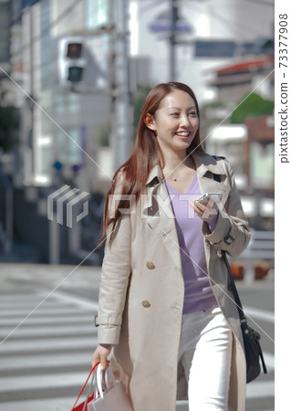 走在步行者的婦女,當拿著智能手機時 走在步行者的婦女,當拿著智能手機時 73377908
