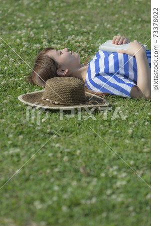 A woman who sleeps on her back with a book in the meadow 73378022