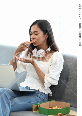 Portrait of young woman enjoy eating pizza while sitting on sofa in living room. 73378136