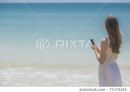 A woman with a smartphone at the beach A woman with a smartphone at the beach 73378265