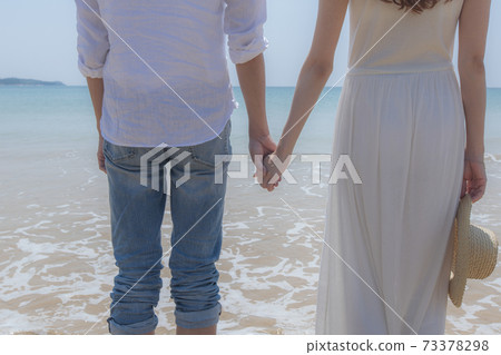 The back of a couple holding hands at the edge of a beach The back of a couple holding hands at the edge of a beach 73378298