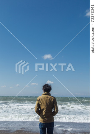 A man's appearance standing on a sandy beach 73378341